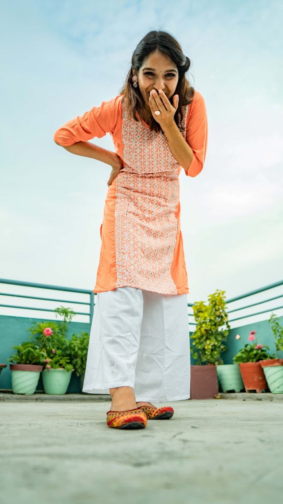 South Asian woman in vibrant kurta laughing on a balcony, showcasing traditional attire and joy.